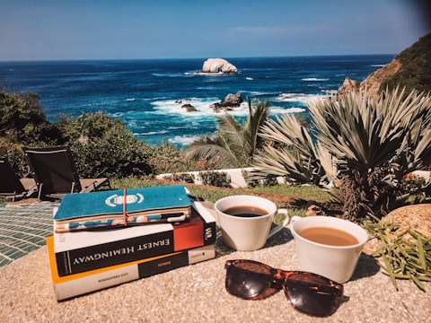 A stack of handwritten journals and a cup of tea by a window with ocean views.