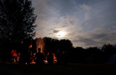 A group of players strategizing around a campfire in a dark, eerie forest setting.