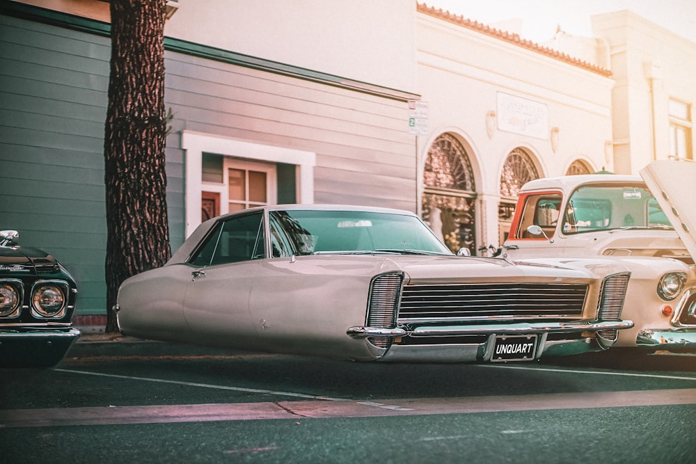 classic white car parked beside white concrete building during daytime