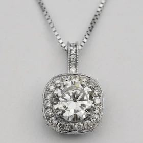 A refined necklace featuring a single radiant diamond pendant resting on a smooth white fabric.