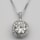 A silver necklace with a round, brilliant-cut diamond pendant surrounded by smaller diamonds arranged in a square halo setting. The pendant is attached to an elegant and delicate silver chain, which complements the sparkle of the diamonds.