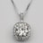 A silver necklace with a round, brilliant-cut diamond pendant surrounded by smaller diamonds arranged in a square halo setting. The pendant is attached to an elegant and delicate silver chain, which complements the sparkle of the diamonds.