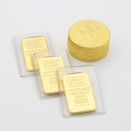 A collection of gold items including stacked Canadian maple leaf coins and several half-ounce fine gold bars labeled 'Credit Suisse' in protective packaging laid on a flat surface.