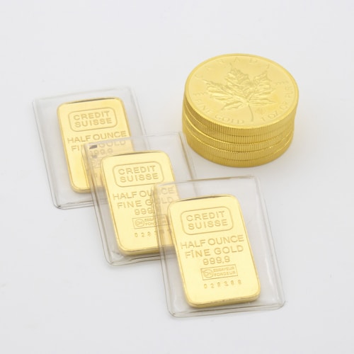 A collection of gold items including stacked Canadian maple leaf coins and several half-ounce fine gold bars labeled 'Credit Suisse' in protective packaging laid on a flat surface.