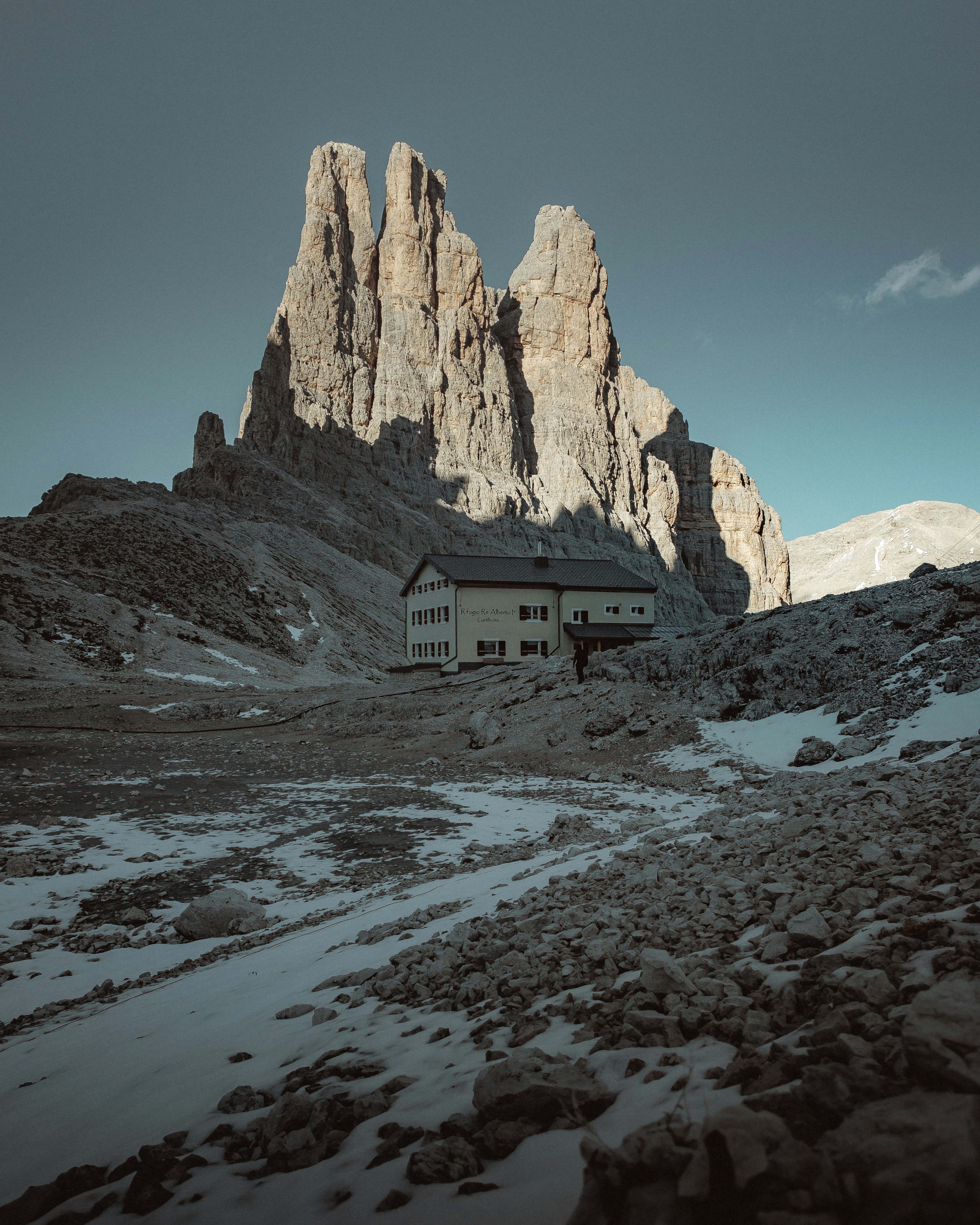 A small mountain hut on a scree slope beneath a pale limestone peak