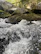 Close-up of hands gently touching moss-covered rocks beside a bubbling creek.