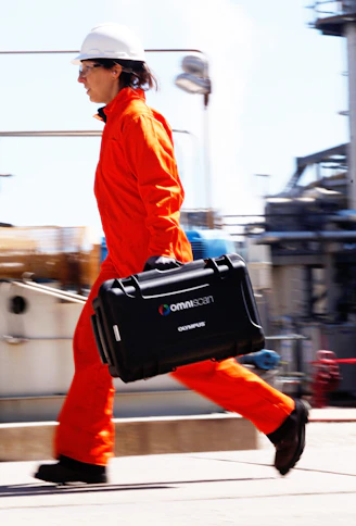 man in orange jacket carrying black luggage bag