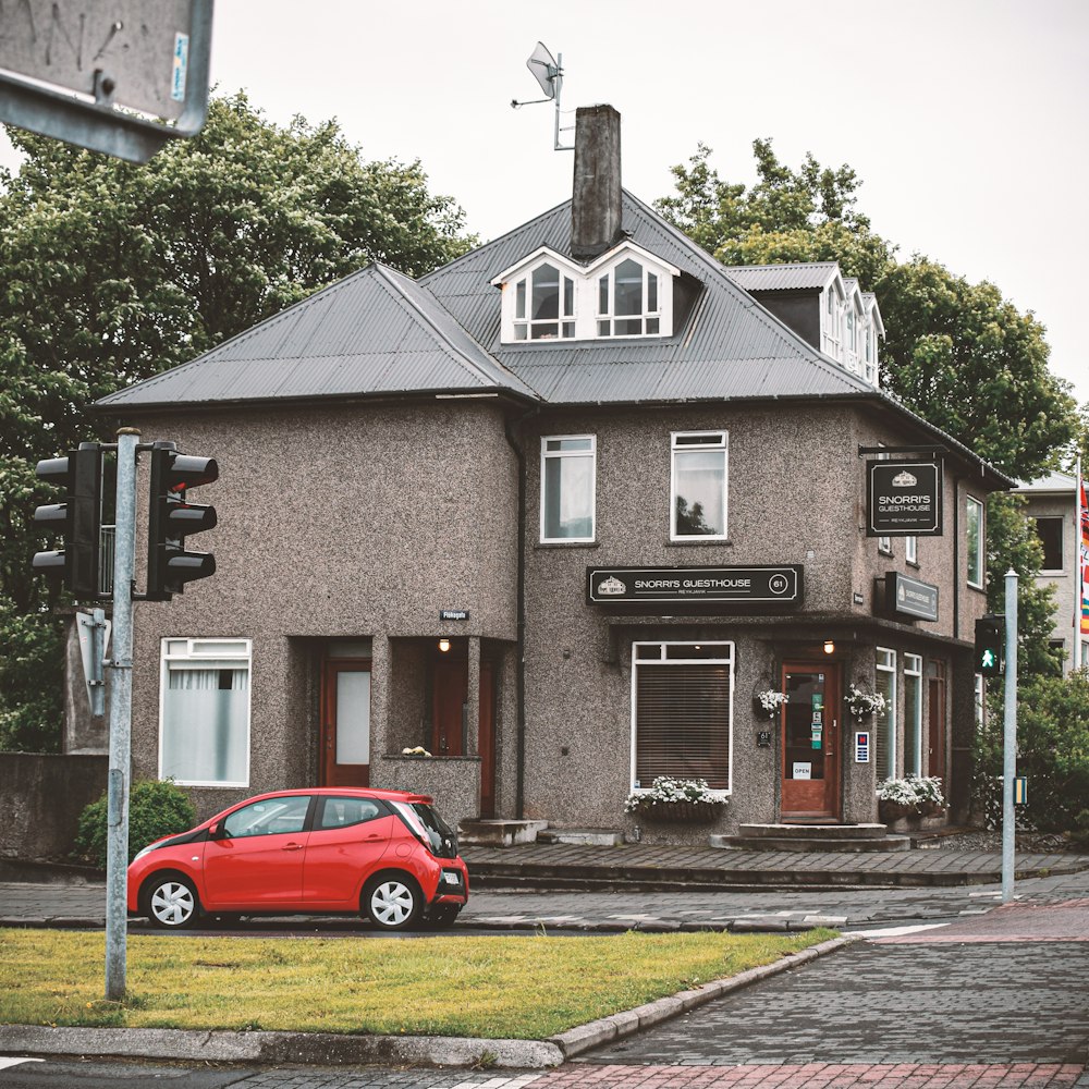 red sedan parked beside brown and white concrete building during daytime