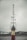 A group of children stand in a line in front of a tall metal tower, with their hands raised in prayer or a symbolic gesture. The background shows overcast skies and a few buildings.