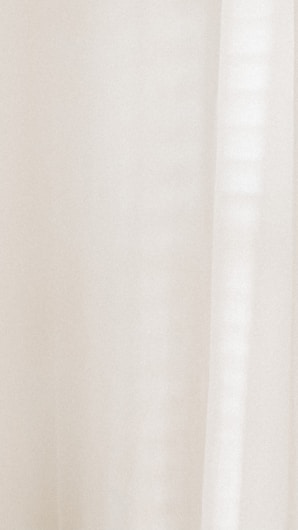 A light-colored fabric with subtle vertical lines, suggesting curtains or drapery. Delicate shadows create a soft and calming visual effect.