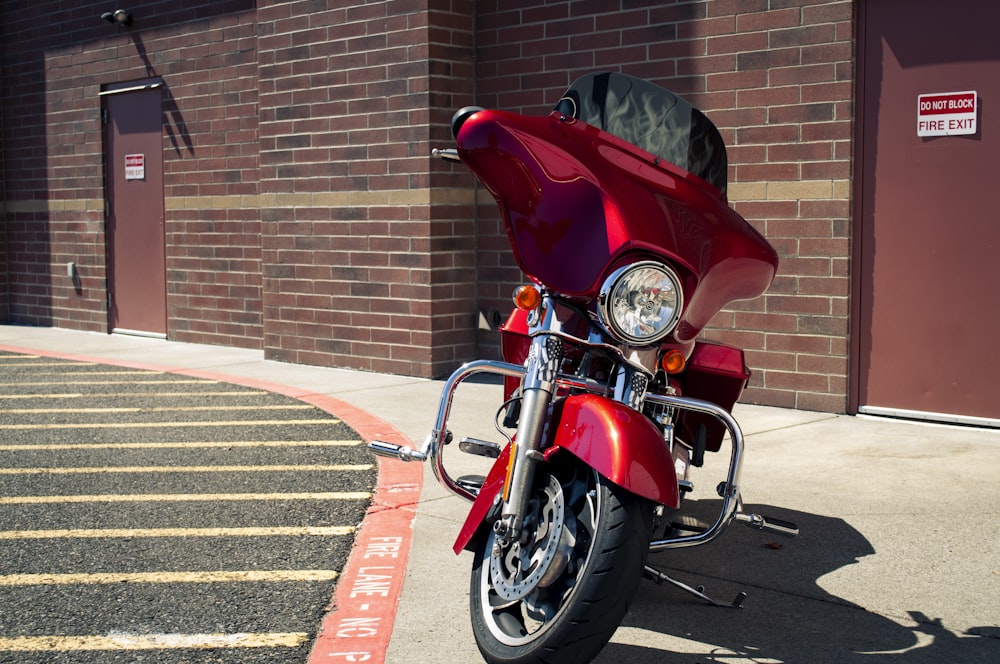 red and silver cruiser motorcycle parked beside brown brick wall