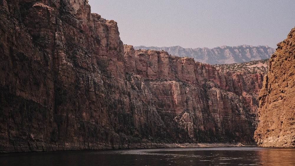 montanha rochosa marrom ao lado do corpo de água durante o dia