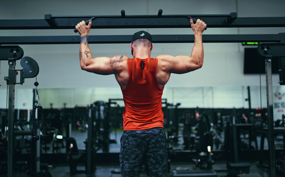 man in red tank top and black shorts holding black and silver barbell