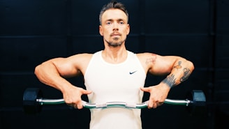 man in white tank top holding gray metal bar