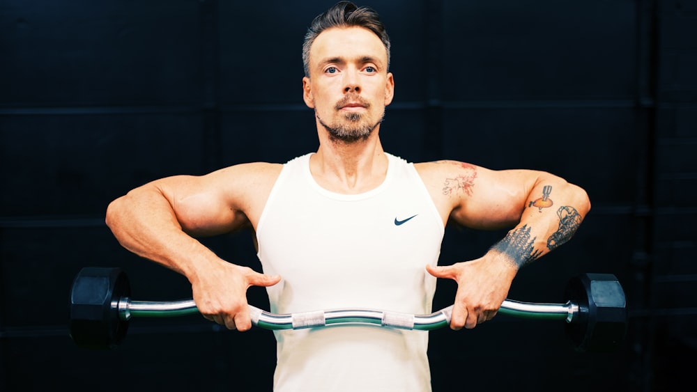 man in white tank top holding gray metal bar