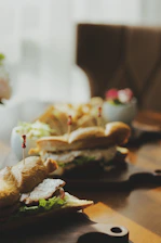 Close-up of a colorful, fresh sandwich served on a wooden board with pickleball paddles resting nearby.