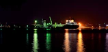 Nighttime shot of a cargo ship illuminated by deck lights against a dark sea.