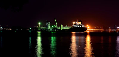 Nighttime shot of a cargo ship illuminated by deck lights against a dark sea.