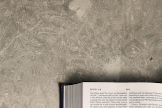 An open book is lying on a textured gray surface. The visible page shows text, which includes a reference to John 3:4. The book's edges and part of the spine are visible at the bottom of the image.