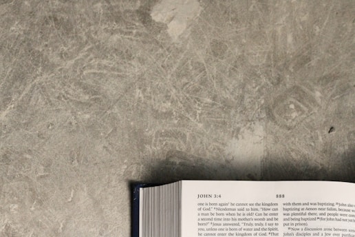 An open book is lying on a textured gray surface. The visible page shows text, which includes a reference to John 3:4. The book's edges and part of the spine are visible at the bottom of the image.