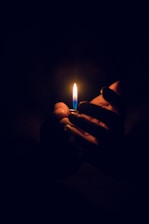 Close-up of a hand holding a small flame glowing warmly in the dark.