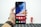 A hand holding a smartphone with a colorful, abstract wallpaper displayed on its screen. The phone interface shows app icons including Google, Play Store, Assistant, and Vsmart. The hand is wearing a brown leather watch. In the blurred background, there is a small figurine resembling a superhero.