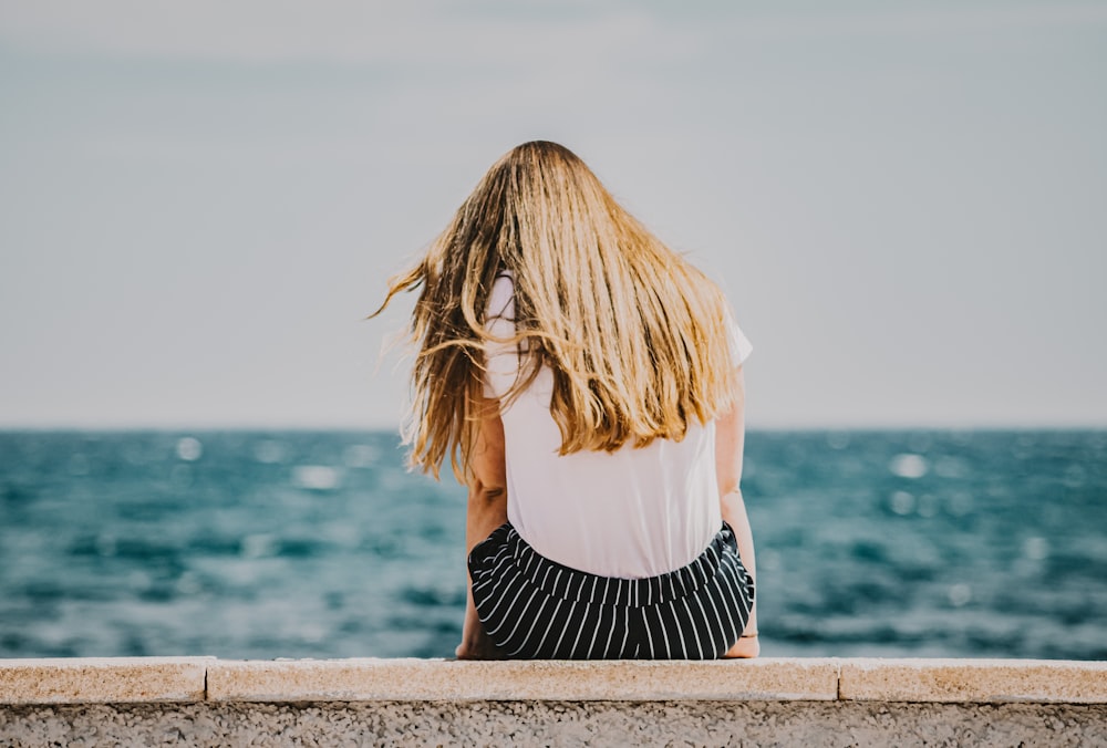 woman in white long sleeve shirt and black and white striped skirt standing on concrete dock