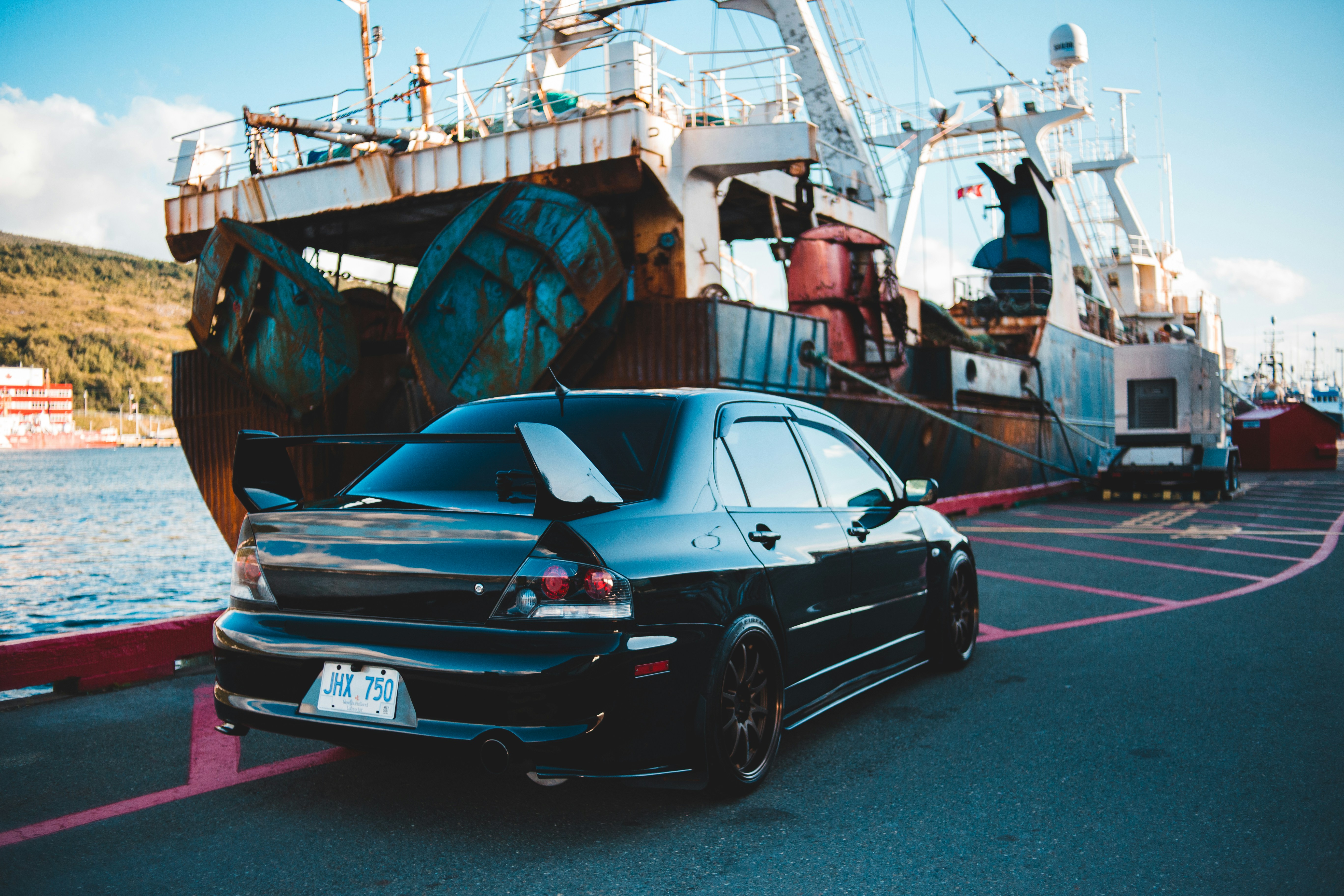 black coupe parked beside white and blue boat during daytime
