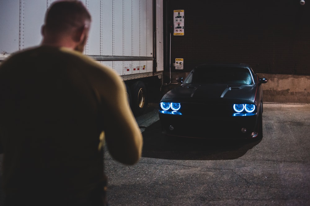 man in black t-shirt standing beside blue car during nighttime