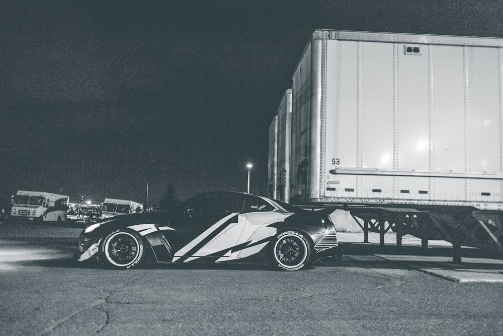 grayscale photo of sports car parked beside truck