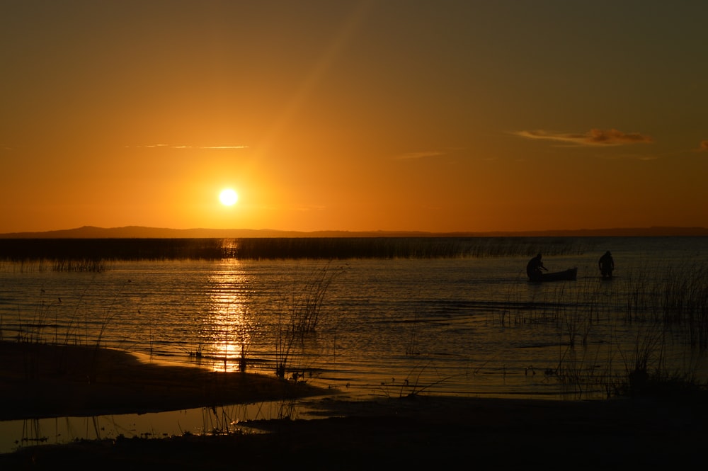 silhouette of person standing on seashore during sunset