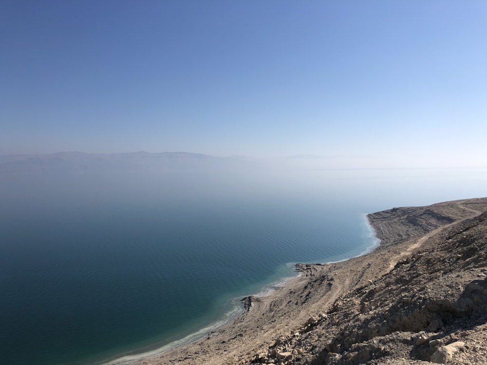 blue sea beside brown mountain under blue sky during daytime