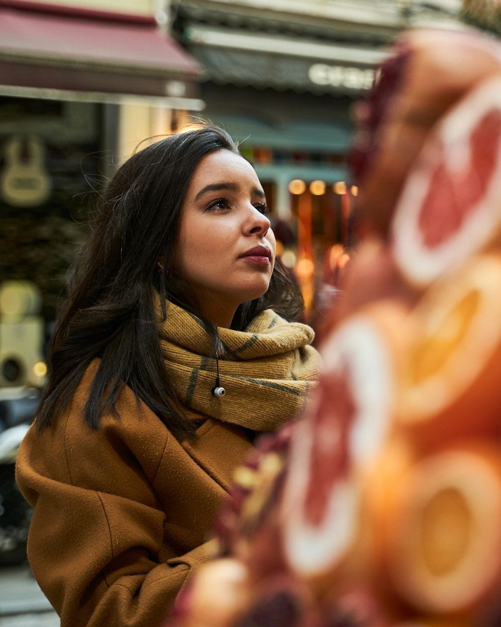 femme en écharpe marron et manteau marron debout près du magasin pendant la journée