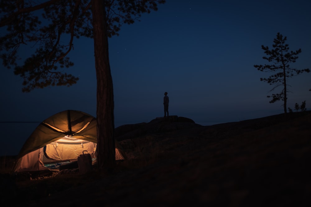 silhouette of person standing on rock near tent during night time