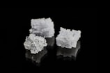 Three crystalline salt cubes are arranged against a sleek black background, showcasing their intricate geometric patterns and reflective surfaces.