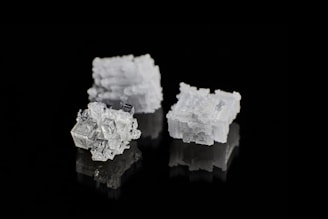 Three crystalline salt cubes are arranged against a sleek black background, showcasing their intricate geometric patterns and reflective surfaces.