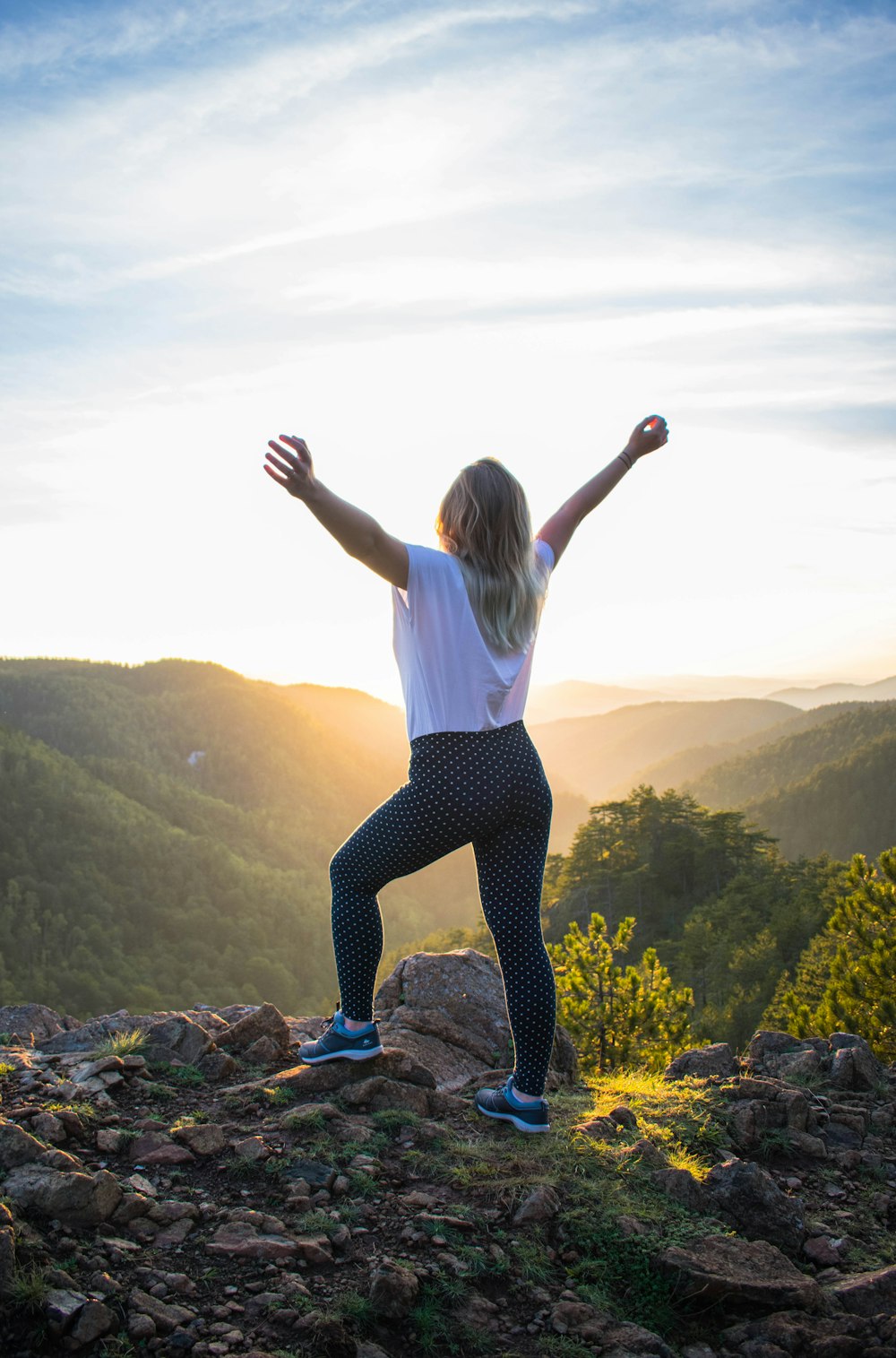 woman in white shirt and black pants standing on rocky mountain during daytime