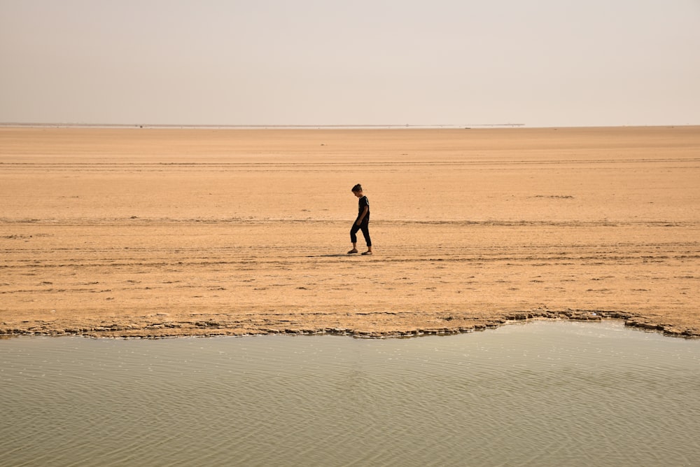 Uomo che cammina sulla sabbia marrone durante il giorno