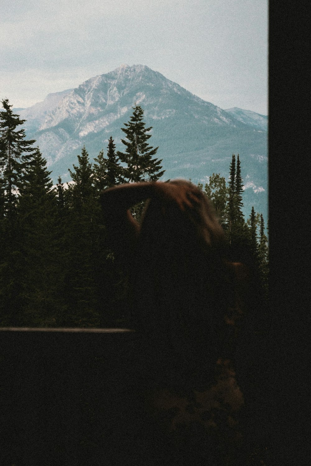 a person looking out a window at a mountain