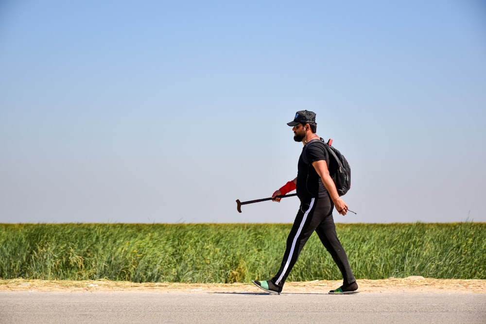 man in black and red jacket and black pants holding black stick walking on brown sand