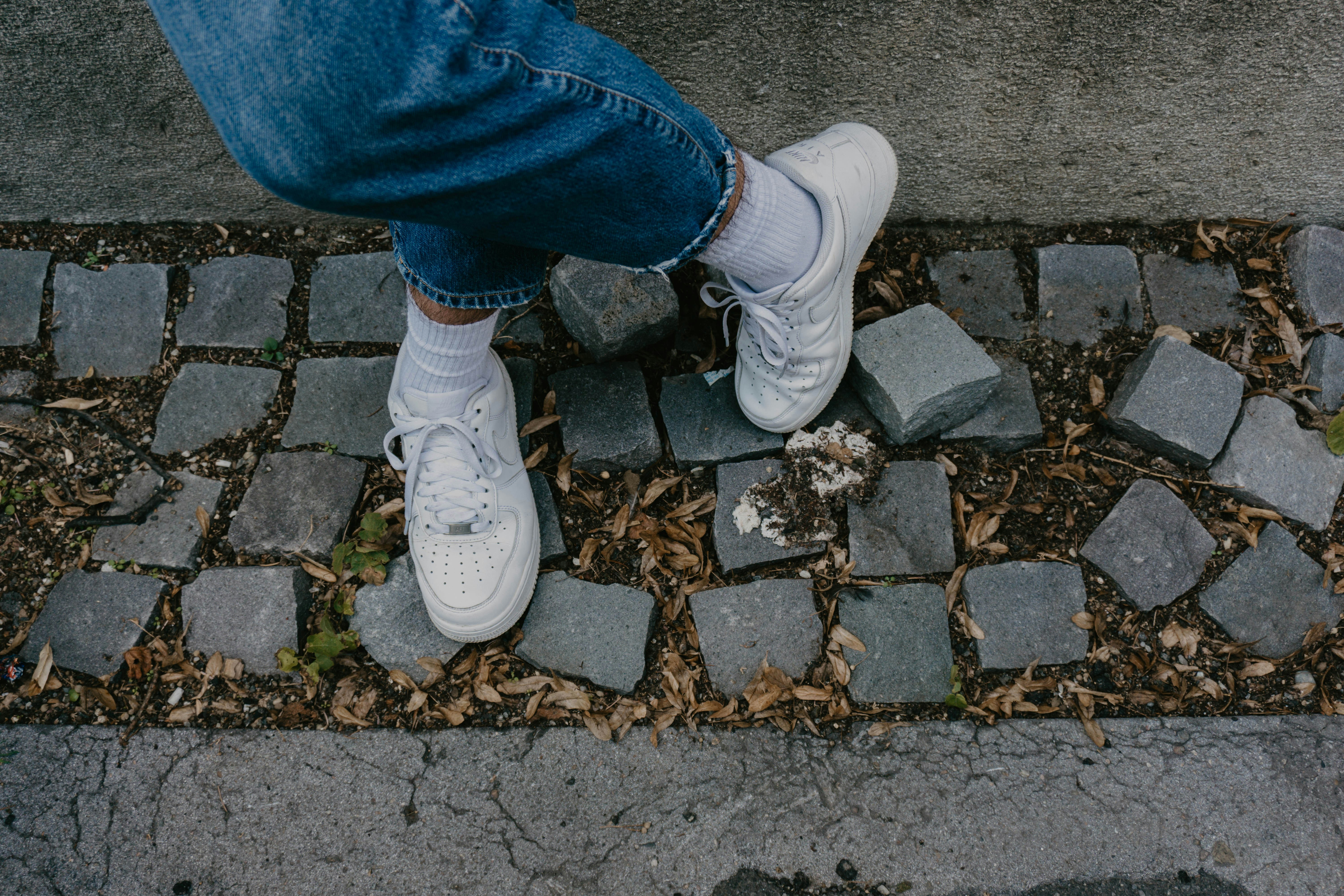 a person wearing white tennis shoes standing on a sidewalk