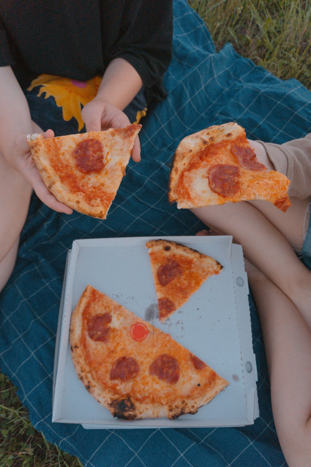 a person sitting on a blanket holding two slices of pizza