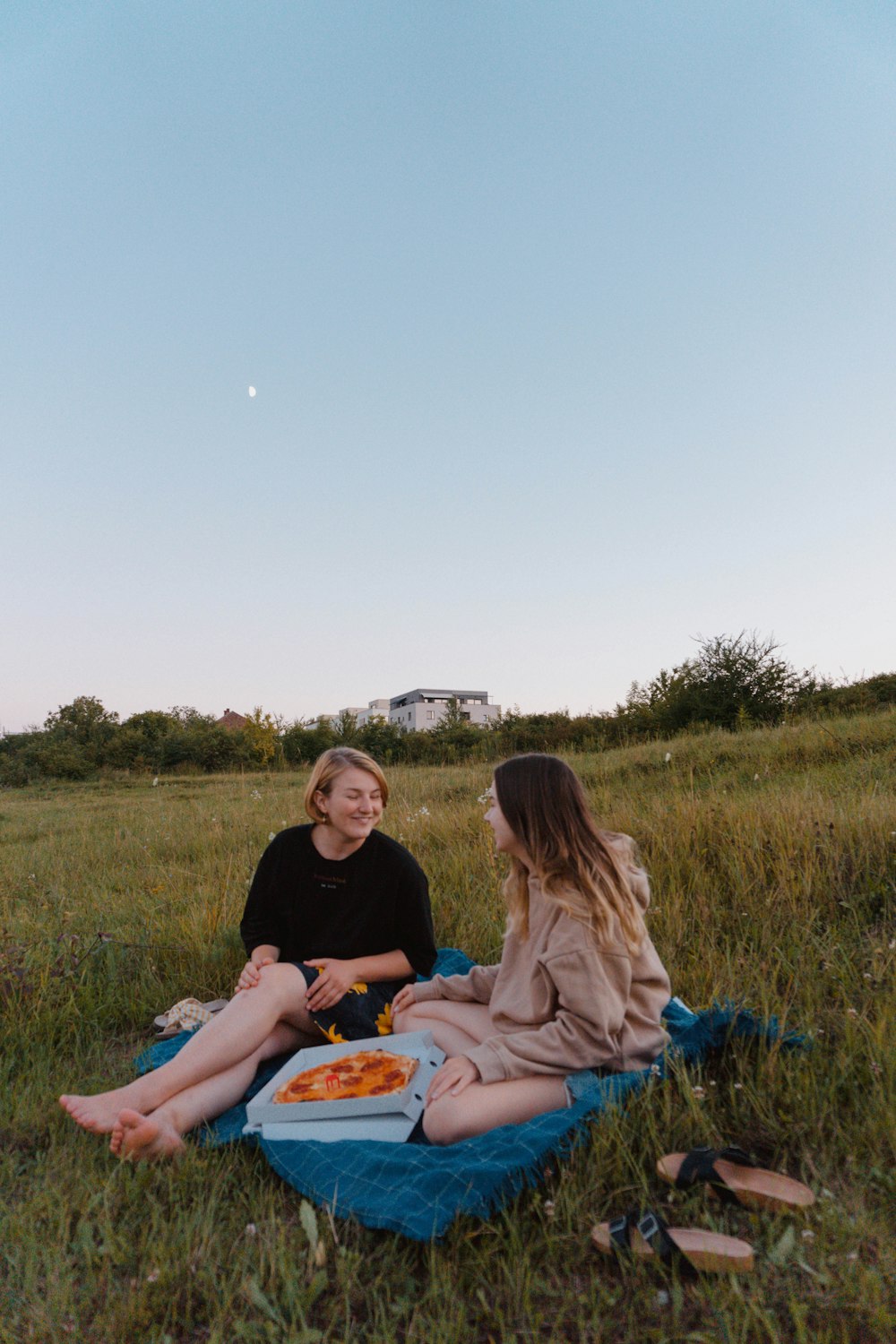 woman in black shirt sitting on grass field beside woman in blue denim jeans during daytime