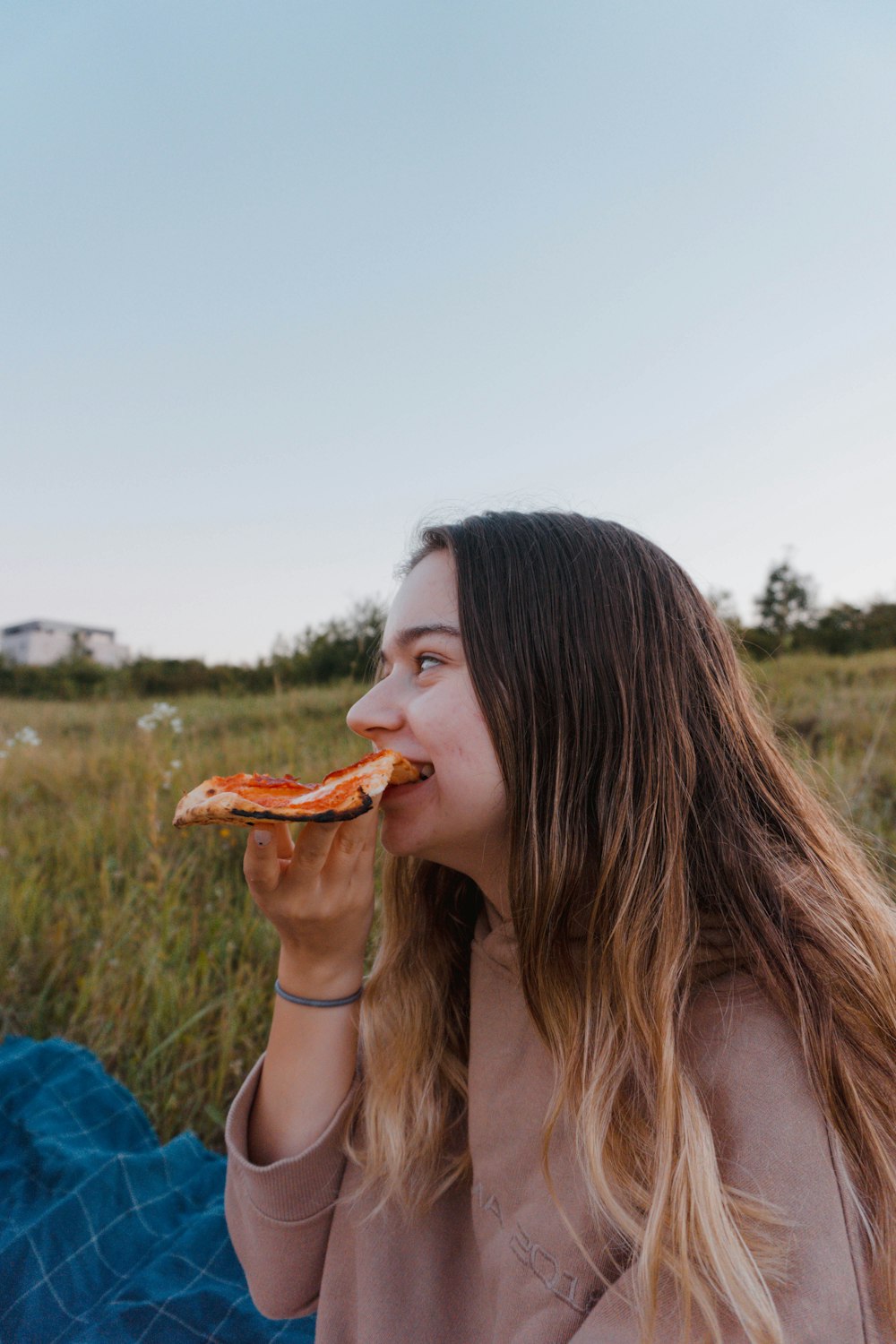 a woman eating a slice of pizza in a field