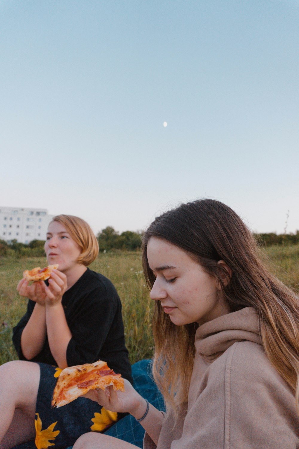 two women sitting in a field eating pizza