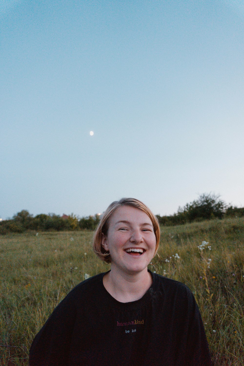 smiling woman in black crew neck shirt standing on green grass field during daytime