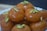 A plate of round, golden-brown sweets garnished with sliced pistachios. The sweets have a shiny, syrupy glaze, suggesting they are a type of dessert.