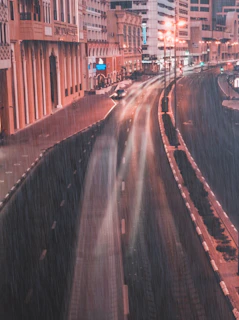 A softly lit photo of a rainy city street with blurred figures passing by.