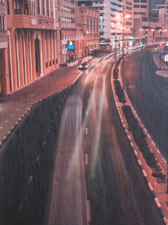 A softly lit photo of a rainy city street with blurred figures passing by.