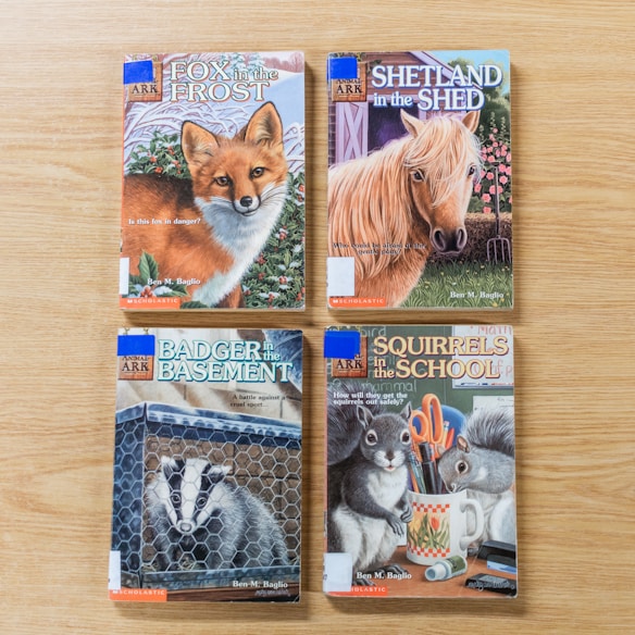 Four children's books are arranged on a wooden surface. Each book cover features an animal and text. The titles include a fox, a horse, a badger, and two squirrels, each illustrated in vibrant colors, emphasizing themes of nature and adventure.